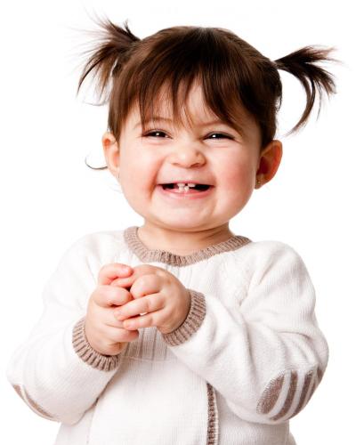 A young girl toddler with four teeth smiling and holding her hands together.